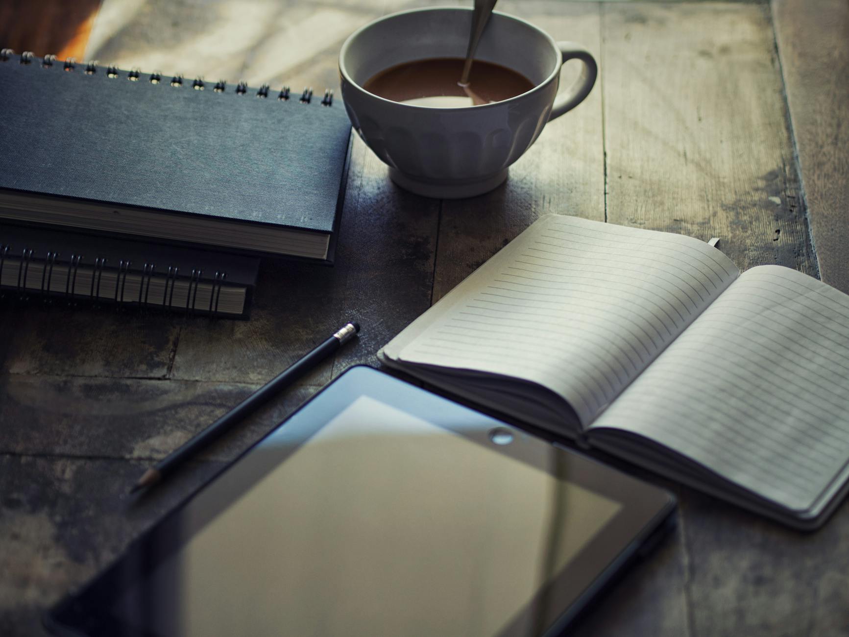 cup filled with coffee near blank journals for freewriting